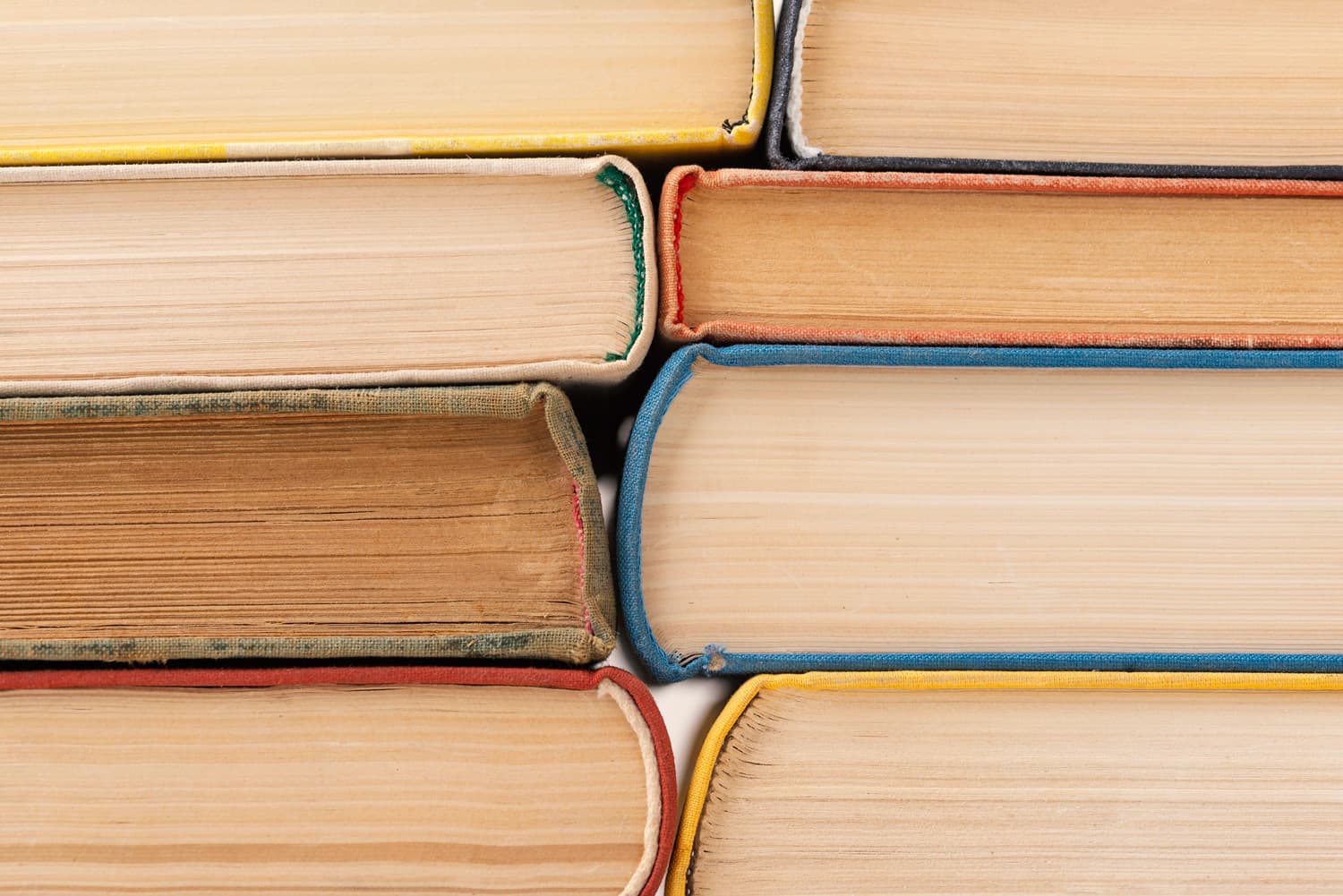 Close-up of two neat stacks of colorful vintage hardcover books, showing the rustic texture of the pages and bindings.