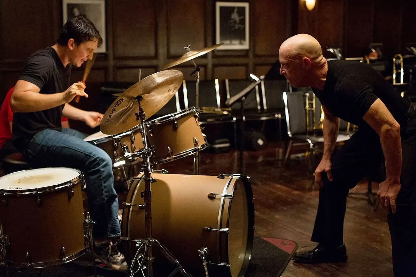 A demanding music instructor closely watches a young drummer during an intense rehearsal, illustrating conflict, pressure, and personal transformation.
